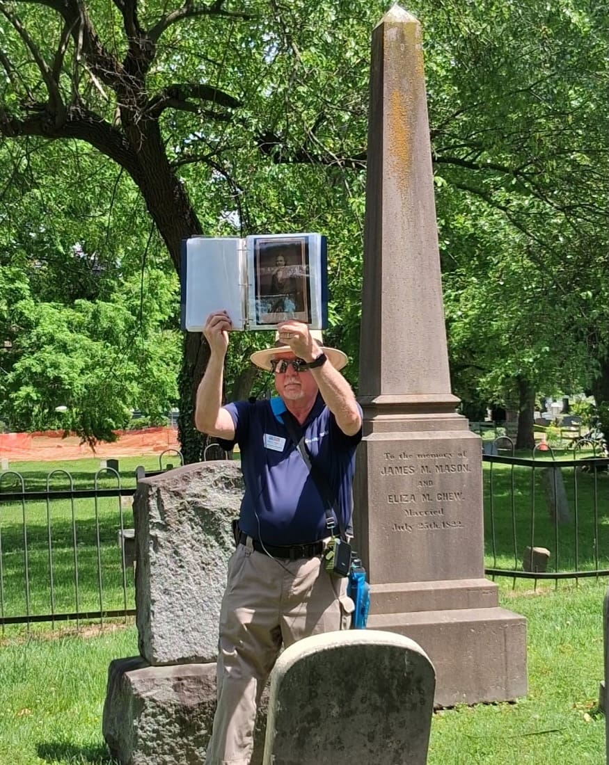David Heiby, who leads Alexandria cemetery tours, holds up a portrait beside the obelisk of James M. Mason in Christ Church Cemetery, Wilkes Street Cemetery Complex