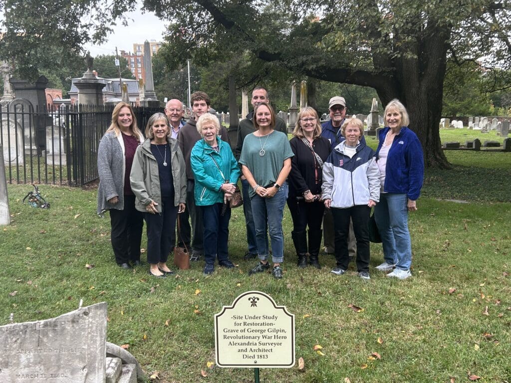 Members of the Anna Maria Fitzhugh Chapter, NSDAR, stand behind the presumed grave of Colonel George Gilpin in the Wilkes Street Cemetery Complex, marked by a sign reading "Site Under Study for Restoration."